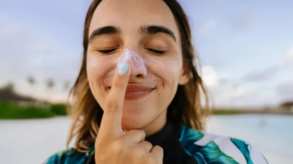 Ilustramos uma mulher passando protetor solar no seu nariz, sorrindo e feliz